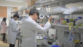 흰색 가운을 입은 남자 2명과 왼쪽에는 분홍색 가운을 입은 여자분이 실험실에서 실험을 하는 모습을 담은 사진