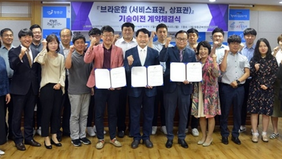 남자 3명이 계약체결장을 손에들고 오른쪽에는 여자1명이 그리고 뒤로는 여러사람이들이 서서 같이 브라운힐(서비스표권, 상표권) 기술이전 계약체결식을 기념하는 모습을 담은 단체사진