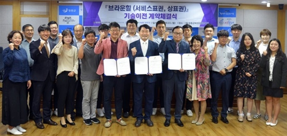 남자 3명이 계약체결장을 손에들고 오른쪽에는 여자1명이 그리고 뒤로는 여러사람이들이 서서 같이 브라운힐(서비스표권, 상표권) 기술이전 계약체결식을 기념하는 모습을 담은 단체사진