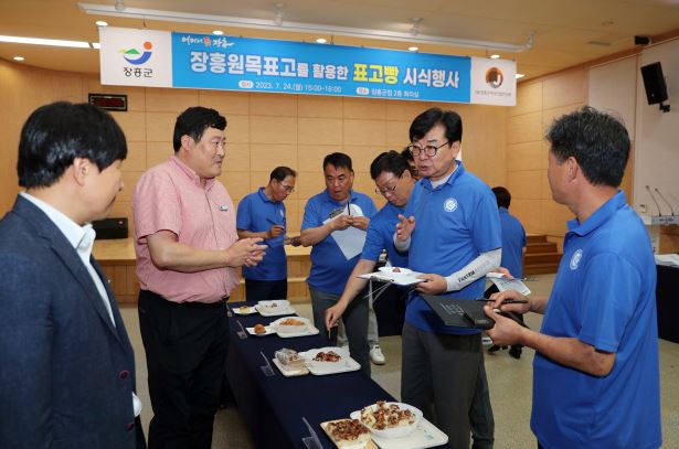 분홍색 옷을 입은 안내원과 파란색 옷을 입은 여러 직원분들과 김성 장흥군수가 빵을 시식하면서 평가하는 모습을 담은 사진