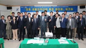 양복을 입은 여성분들과 남성분들이 무대 앞에 나와 장흥 생물의약산업 통합 협의회 워크숍을 개최식을 기념하기 위한 단체 사진