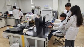 연구실에서 하얀색 가운을 입고있는 남자 2명이 모니터를 보는 모습과 하얀색 가운을 입은 남자 1명이 컴퓨터를 만지고 뒤에는 하얀색 가운을 입은 남자 1명과 여자 1명이 그를 지켜보고 있는 모습을 담은 사진